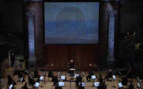 A socially-distanced orchestra performs in an eerily lit LSO St Luke's
